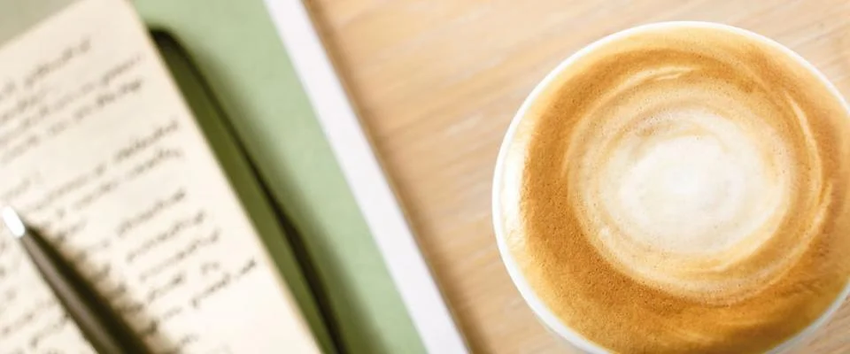 Kop schuimende koffie naast een notitieboekje - Nestlé Professional