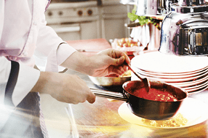 Handen scheppen rode saus uit steelpan en scheppen deze op een gerecht - Nestlé Professional