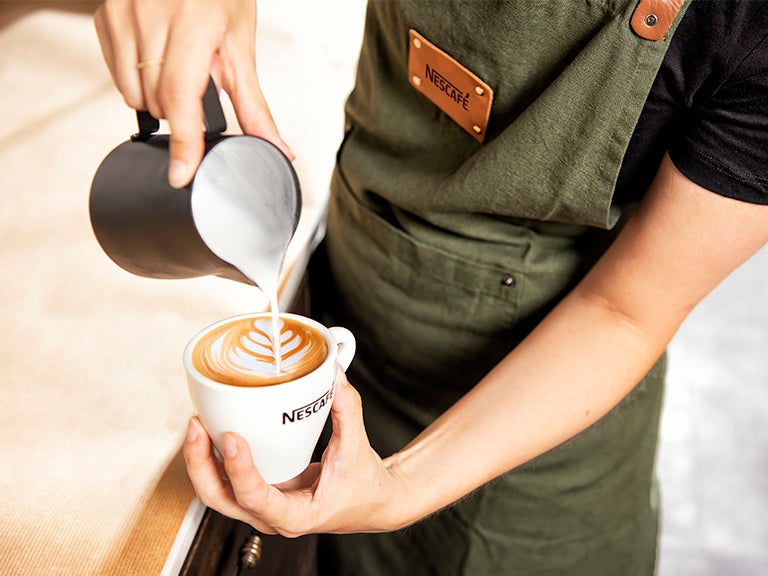 Barista tekent met melk een figuur in een kopje Nescafé koffie - Nestlé Professional