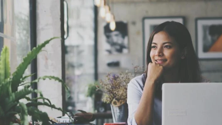 Vrouw aan het werk op haar laptop in een café en kijkt uit het raam - Nestlé Professional