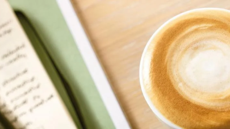Kop schuimende koffie naast een notitieboekje - Nestlé Professional