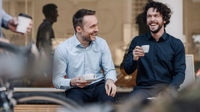 Volwassenen in pakken zitten glimlachend en drinken koffie.
