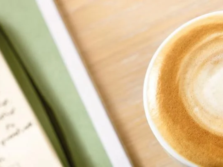 Kop schuimende koffie naast een notitieboekje - Nestlé Professional