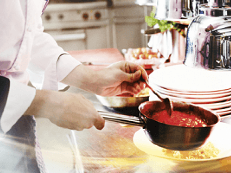 Handen scheppen rode saus uit steelpan en scheppen deze op een gerecht - Nestlé Professional