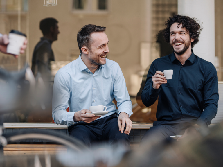 Volwassenen in pakken zitten glimlachend en drinken koffie.