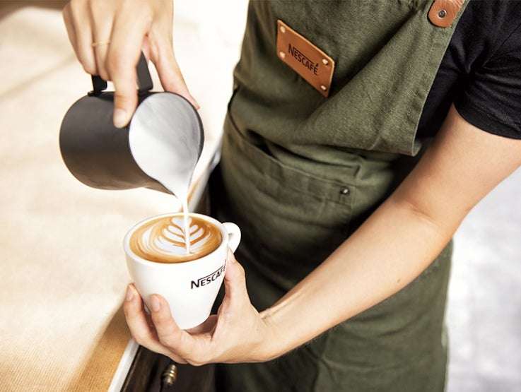 Barista tekent met melk een figuur in een kopje Nescafé koffie - Nestlé Professional