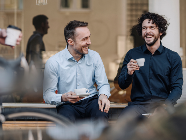 Volwassenen in pakken zitten glimlachend en drinken koffie.