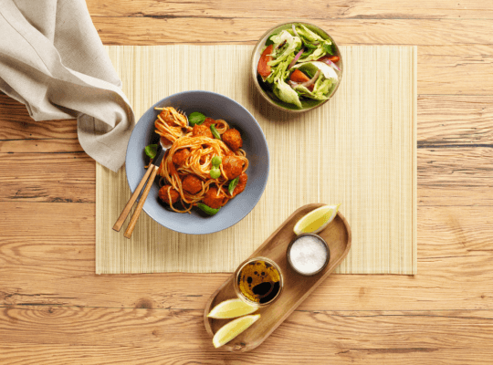 Een kom noedels en salade op een tafel