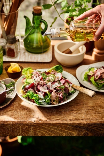 Een persoon die olijfolie giet op een salade met radijs