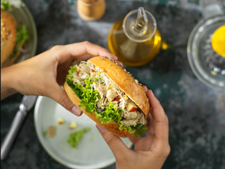 Een persoon die een sandwich met tonijn over een wit bord houdt