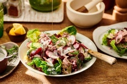 Een persoon die olijfolie giet op een salade met radijs