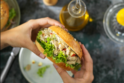 Een persoon die een sandwich met tonijn over een wit bord houdt