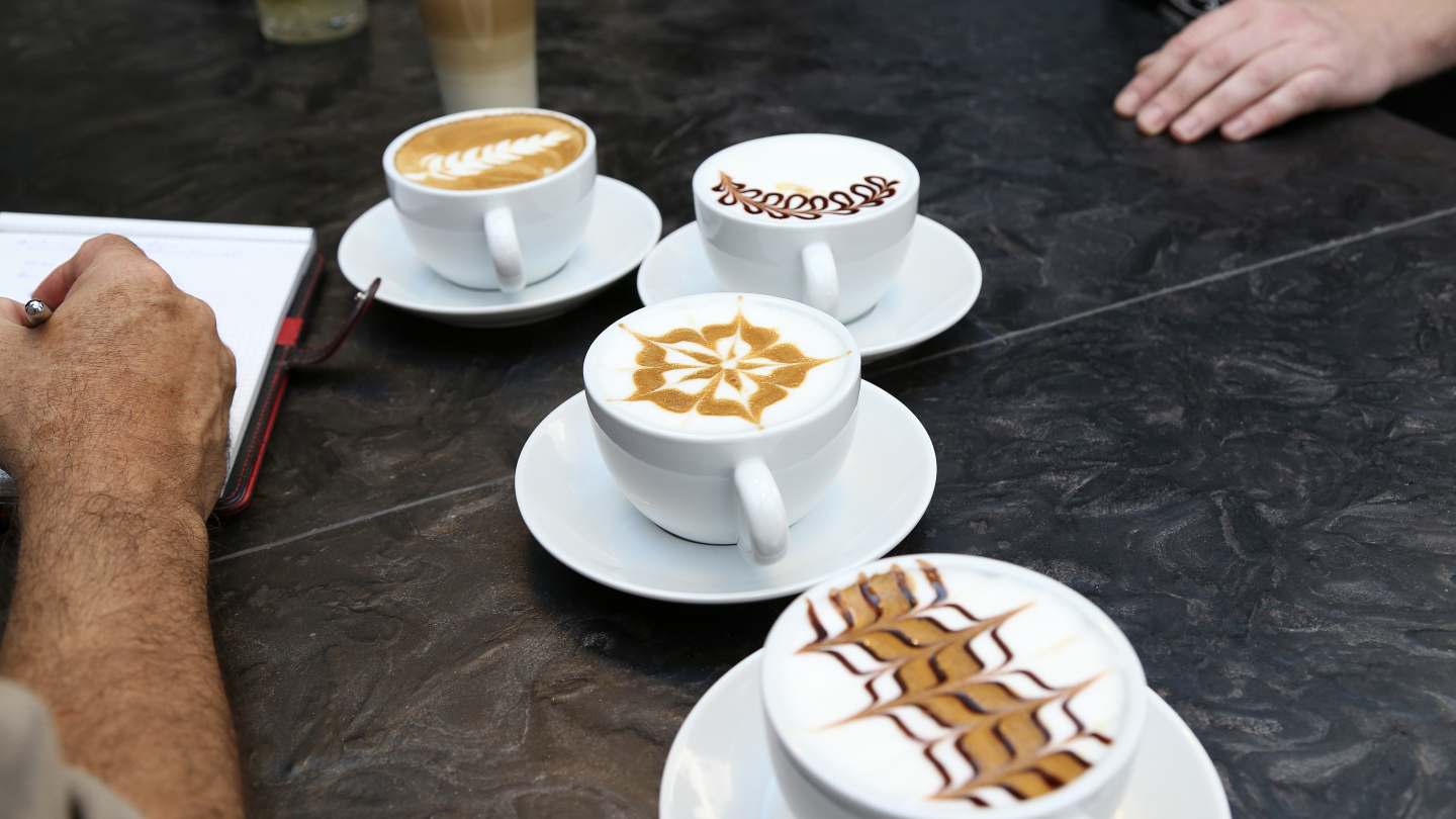 Tafel met meerdere kopjes koffie met figuren in het melkschuim - Nestlé Professional